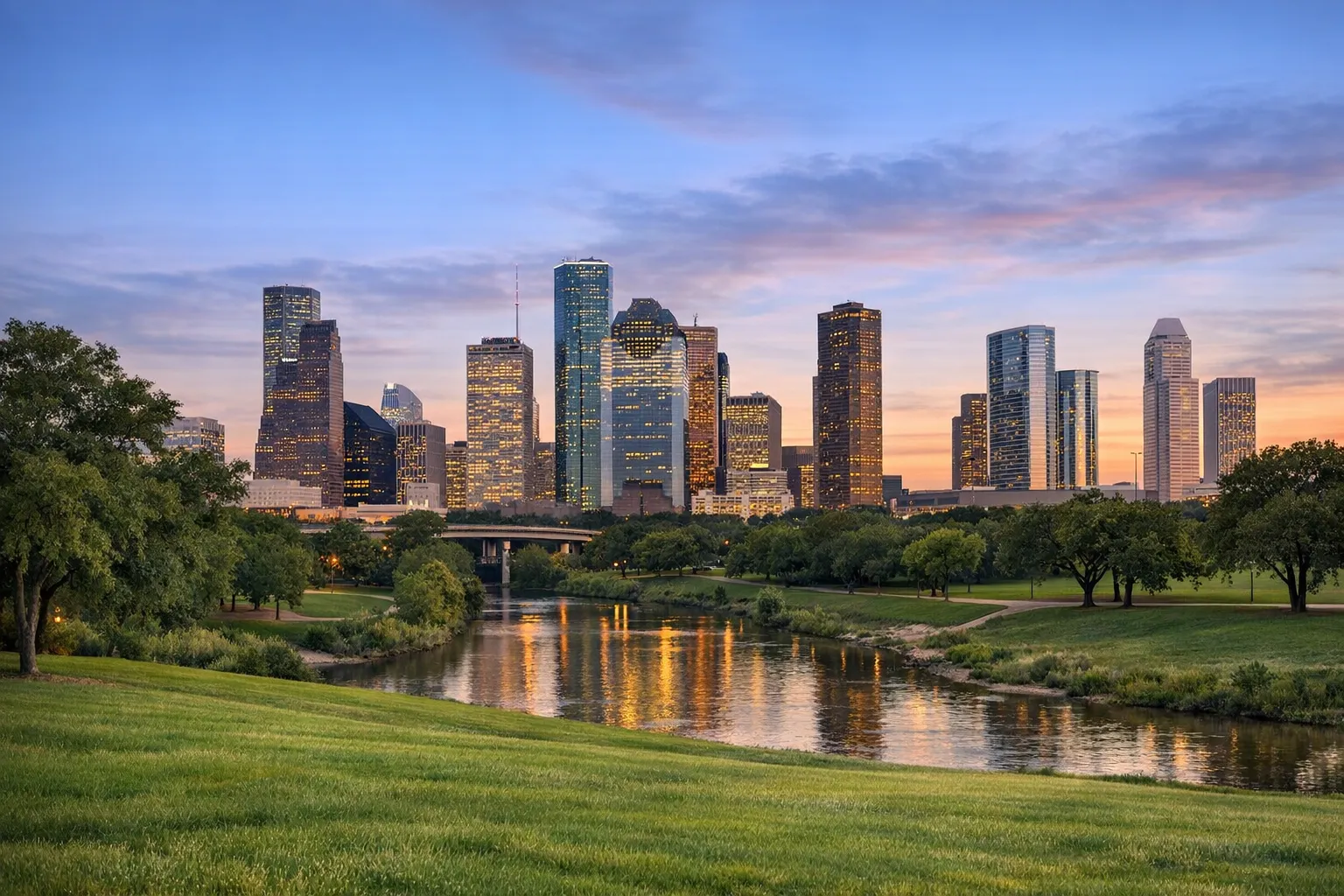 The downtown Houston skyline seen across the green banks of Buffalo Bayou.