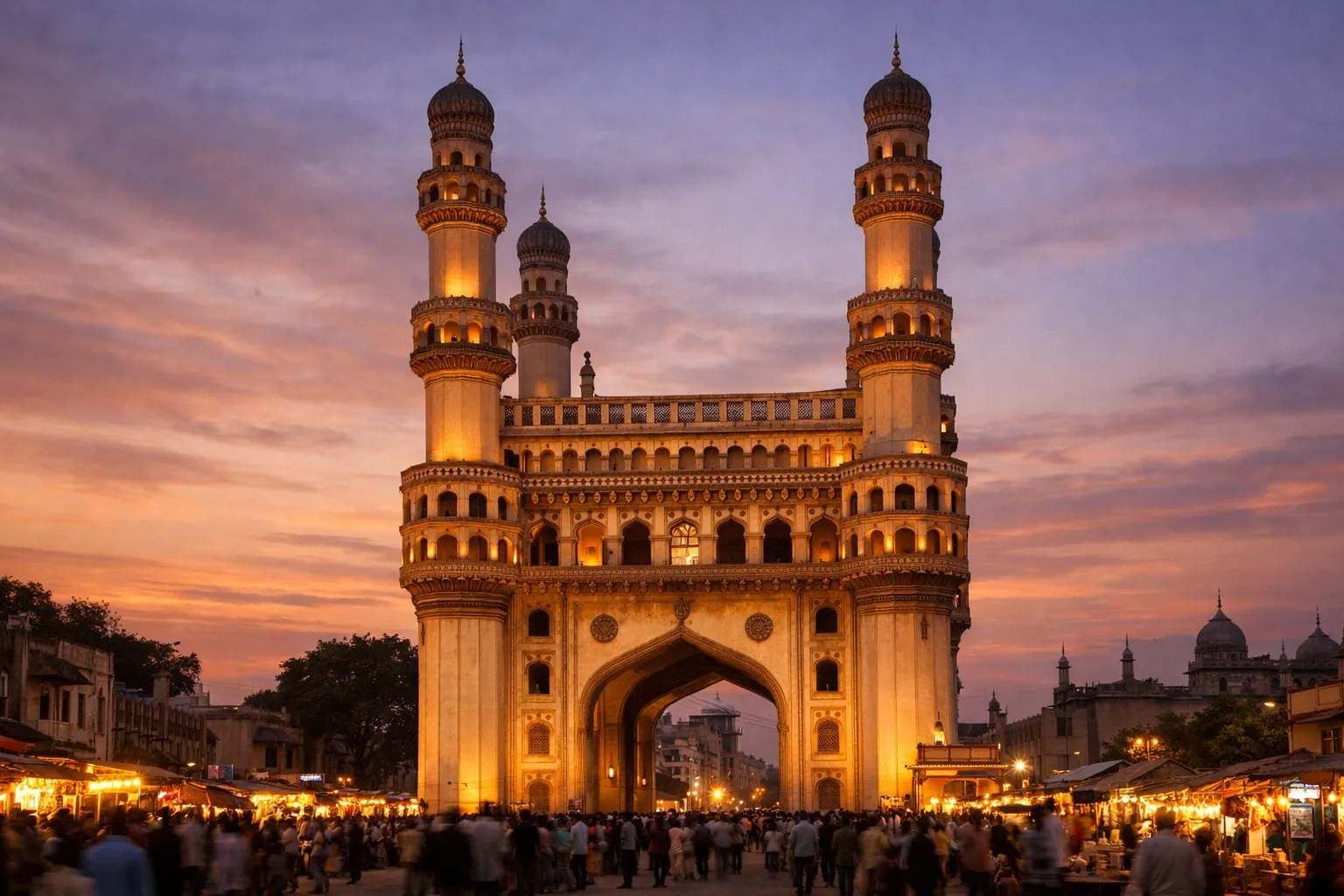 The four illuminated minarets and arches of the Charminar monument against a dusk sky.